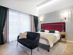 A hotel room with a bed, a black armchair, a nightstand, and a window with curtains. - Hotel Golden Queen (Kraków)