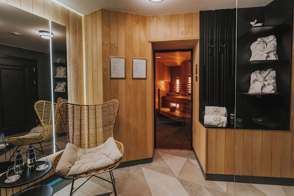 Un hall d'hôtel avec des boiseries, des fauteuils en osier, un comptoir d'accueil et un mur noir orné de serviettes et d'une enseigne.