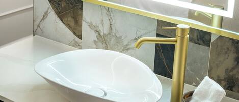 Une salle de bain avec un lavabo blanc, des robinetteries dorées, un miroir à cadre rond et une tête de lit rouge.