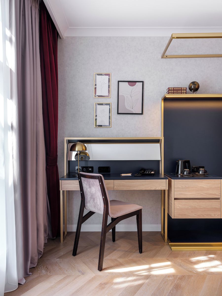 A modern hotel room with a wooden desk, a chair, a bed, and a bedside table.
