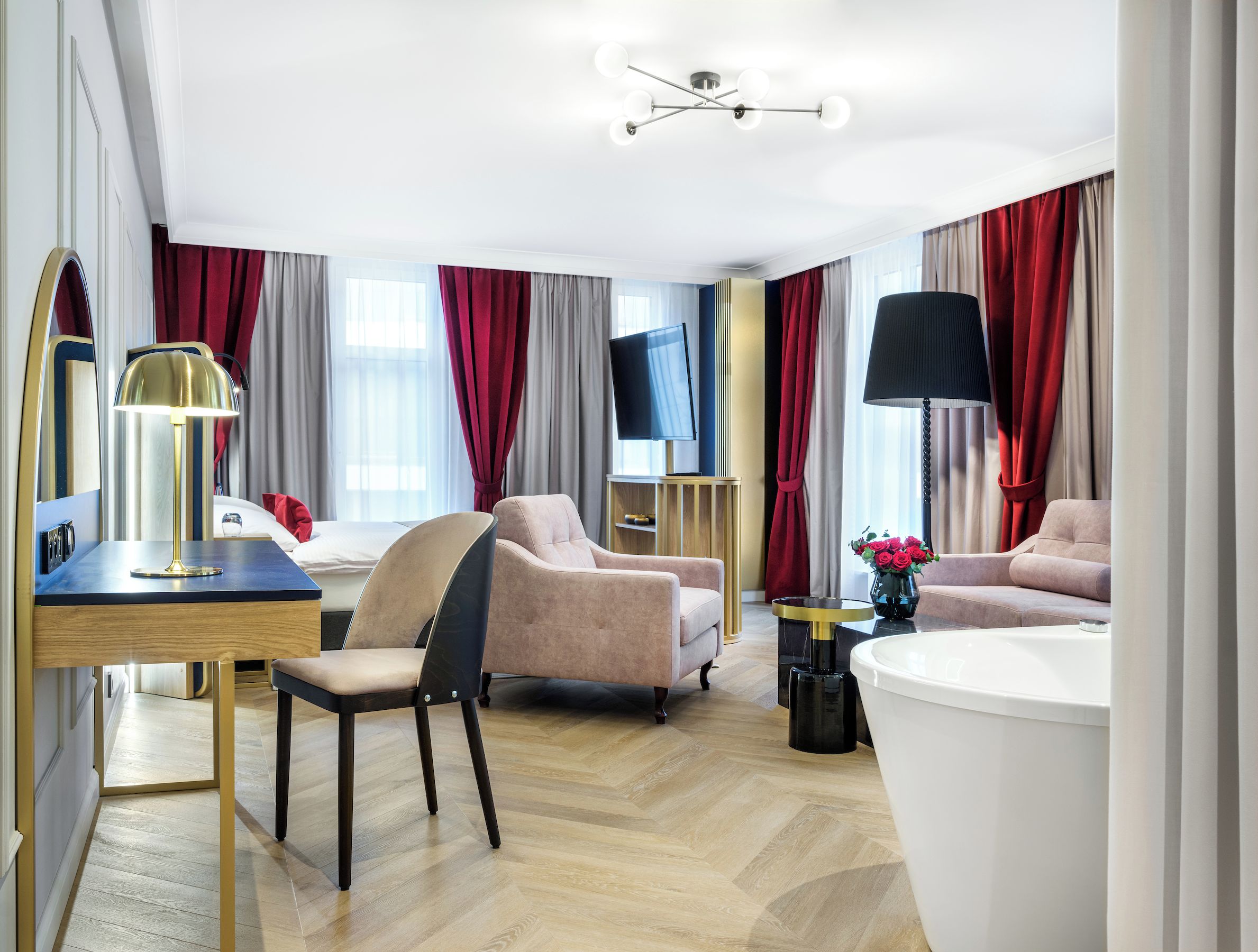 Habitación de hotel moderna con una cama grande, dos sillones, un escritorio con lámpara, un televisor y un baño con bañera.