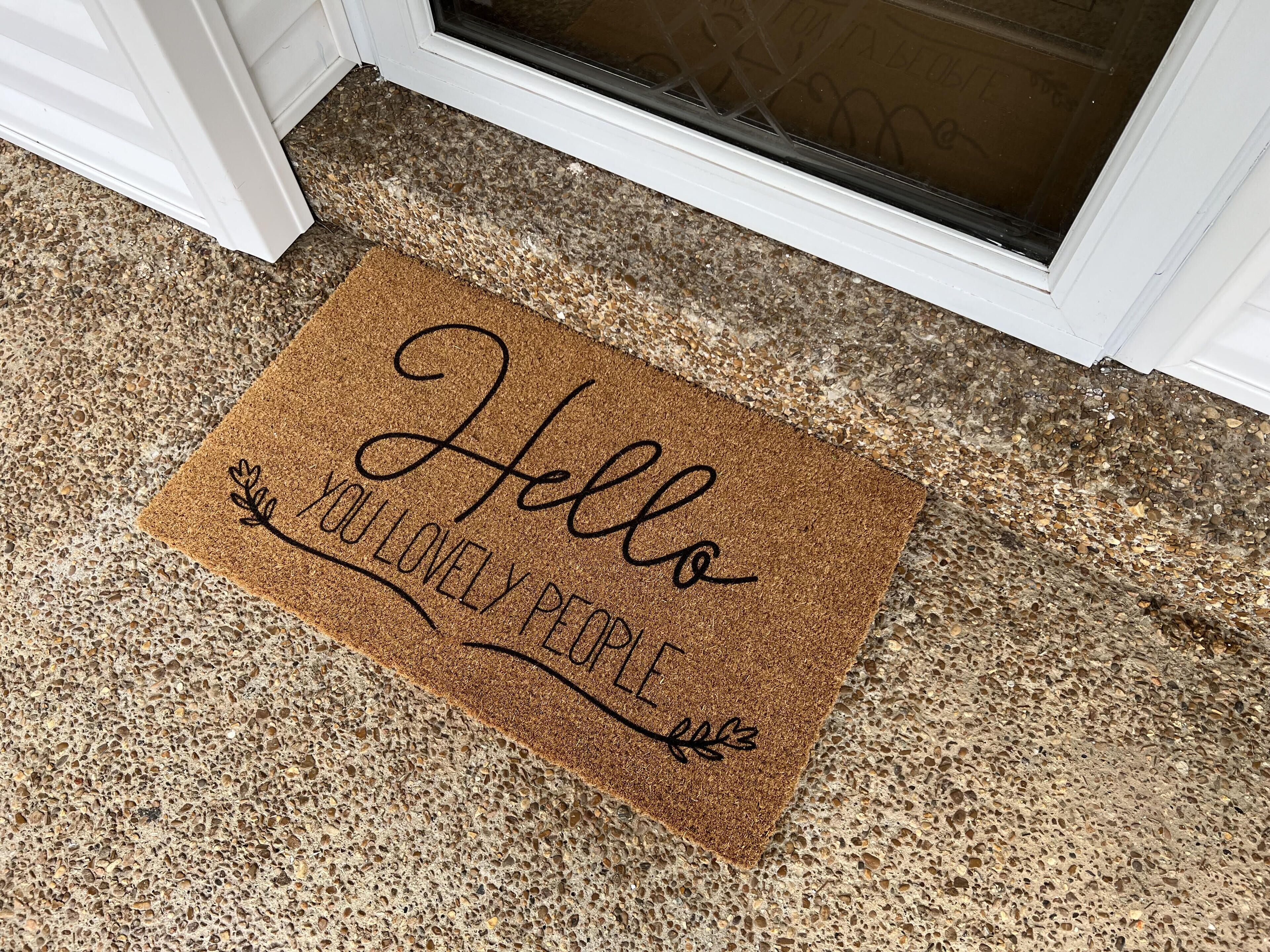 A brown doormat with the text "Hello YOU LOVELY PEOPLE" placed at a door entrance.