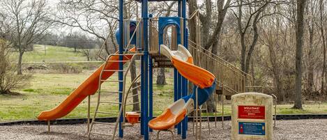 Un parque infantil con un módulo de juegos azul, dos toboganes naranjas y un cartel con instrucciones de seguridad.