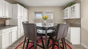 Un coin repas avec une table ronde, quatre chaises, un vase de fleurs et des meubles blancs.