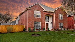Une maison à deux étages, construite en briques, avec une entrée à l’avant, un porche couvert et une pelouse bien entretenue.