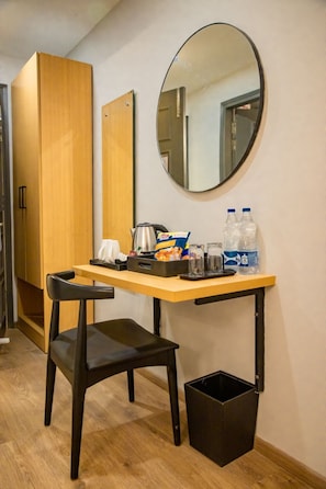 A compact room with a wooden desk, a black chair, a round mirror, and a small trash bin. - Goldenkeys Inn (New Delhi)