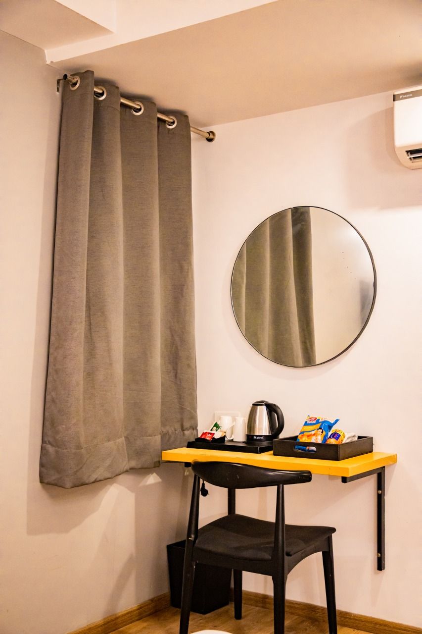 A small room with a single bed, a round mirror, a table with a kettle, and a chair.