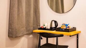 A small room with a single bed, a round mirror, a table with a kettle, and a chair.