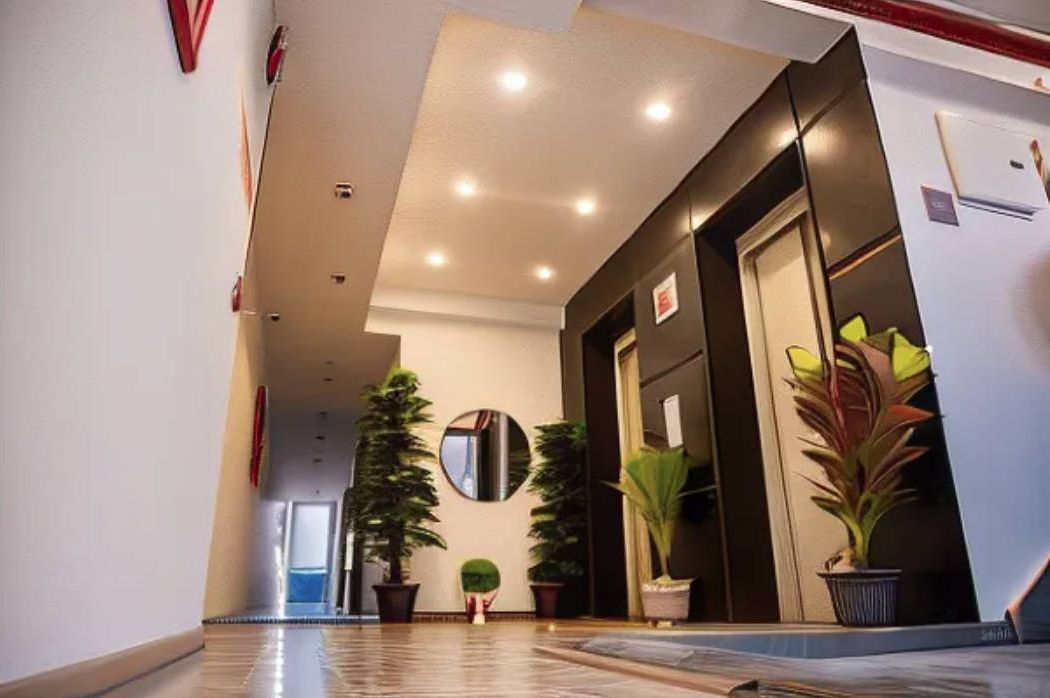 Um saguão de hotel com piso lustroso, um balcão de recepção, plantas em vasos e um espelho grande na parede.