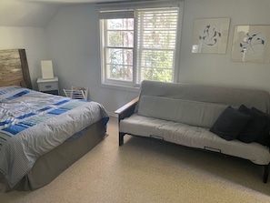 Un dormitorio con cama, sofá, ventana con persianas y cuadros en la pared.