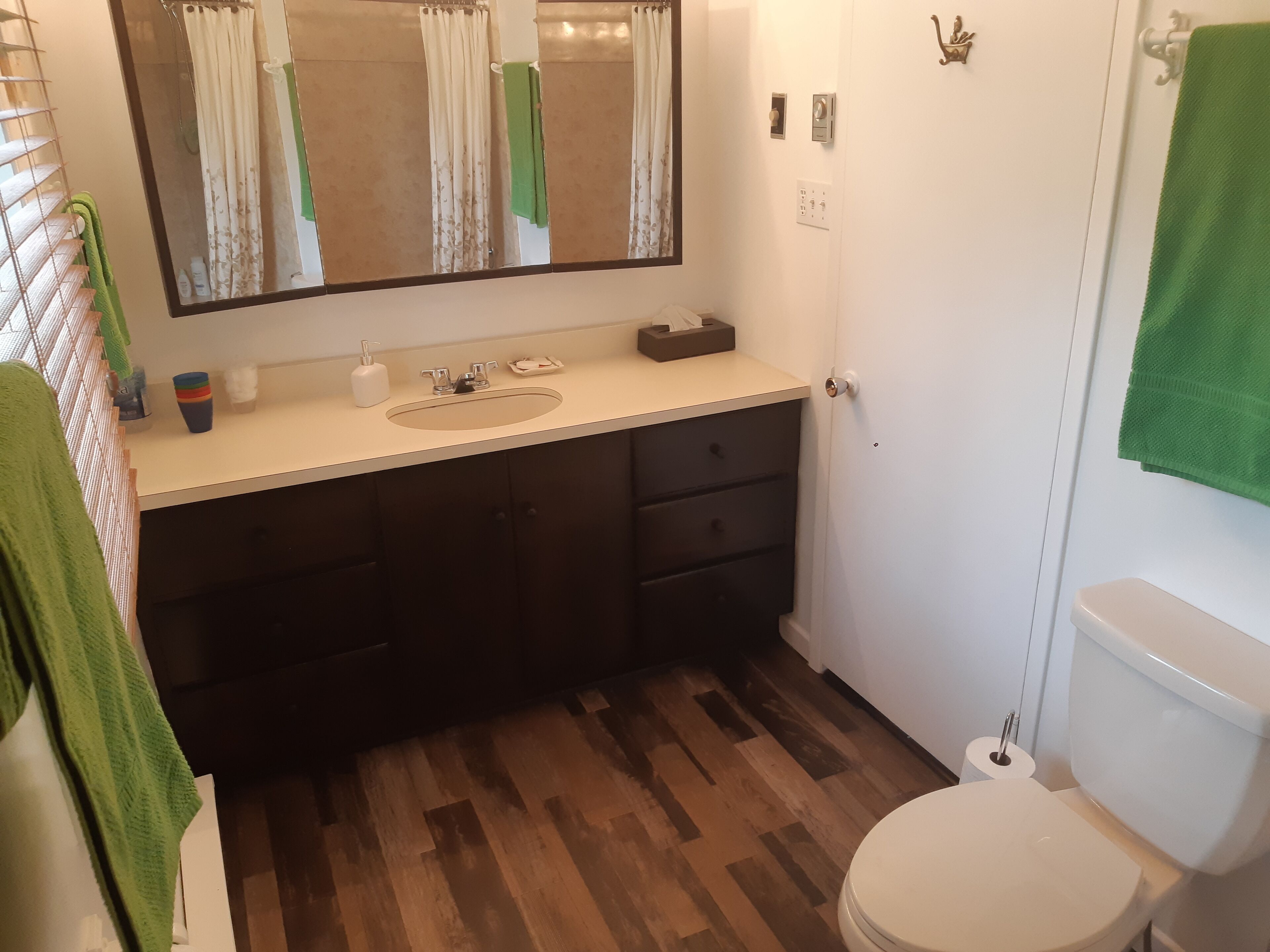 A bathroom with a wooden floor, a sink with a mirror above it, a toilet, and a green towel hanging on the wall.