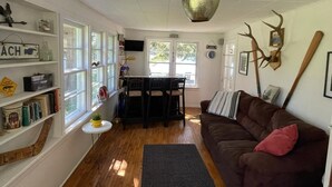 A cozy living room with a brown sofa, a dining table with chairs, a bookshelf, and a large decorative vase.
