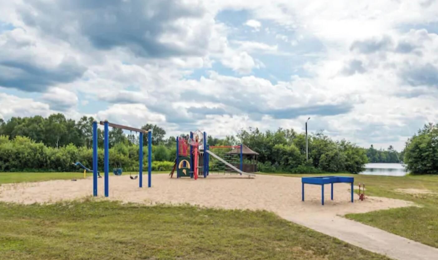 A playground with a slide and climbing structures, a blue table, and a path leading to a body of water.