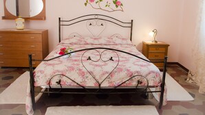 Une chambre à coucher comprenant un lit, une commode, une table de chevet, un miroir et un motif floral décoratif sur le mur.