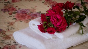 Une serviette blanche ornée d’un bouquet de roses rouges, posée sur une couvre-lit à motifs floraux.