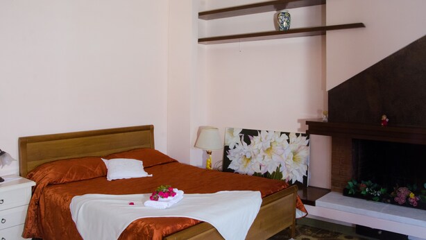 Un lit bien fait, recouvert d’une couvre-lit blanche et orange, une table de chevet avec une lampe, et une étagère fixée au mur au-dessus du lit.