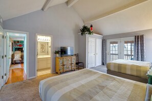 Un dormitorio con una cama grande, televisión, aparador y una puerta que da a otra habitación.