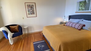 Une chambre à coucher comprenant un lit, une chaise, une petite table, une lampe sur pied, un luminaire au plafond et une fenêtre.