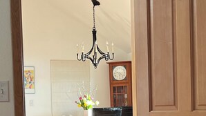 Une pièce comprenant un lit, un fauteuil bleu, une porte en bois, un lustre, une horloge et un vase avec des fleurs.