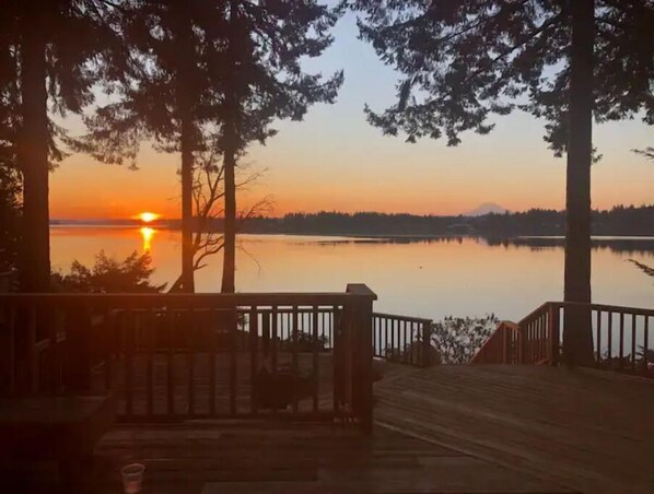A wooden deck with a railing overlooking a calm lake at sunset.
