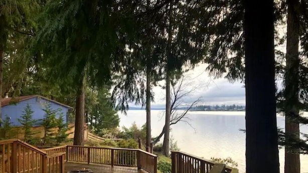 Une terrasse en bois dotée d’une rambarde, offrant une vue sur un lac dont on aperçoit la rive au loin.