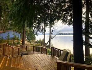 A wooden deck with a railing, overlooking a lake with a distant shoreline.