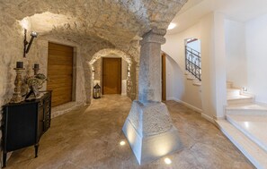 A stone-walled hallway with a wooden door, a stone column, and a staircase with a metal railing. - Luxurious home in Bribir with sauna (Bribir)