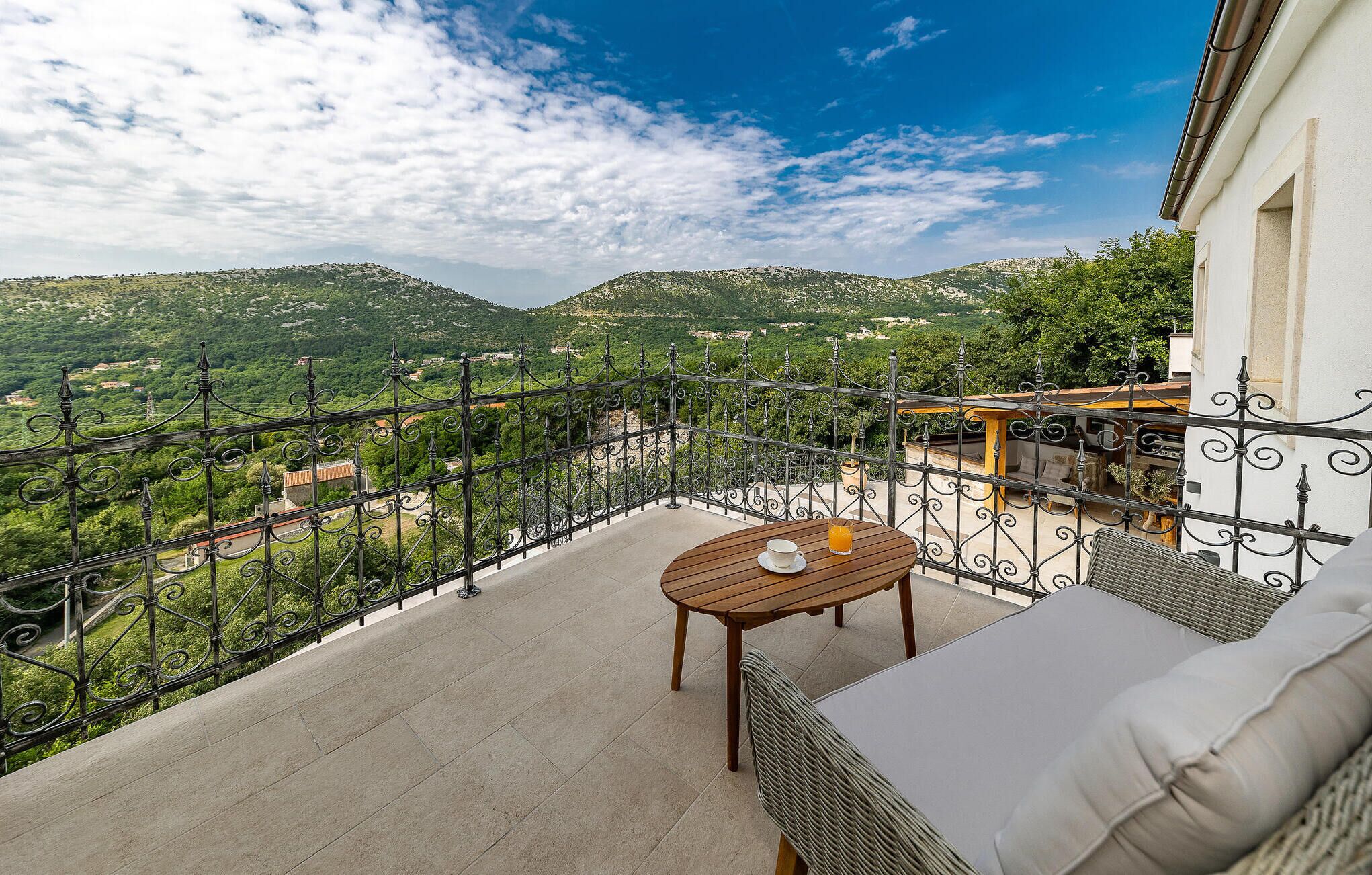 Un balcon avec une table en bois et un canapé en osier, offrant une vue sur un paysage montagneux.