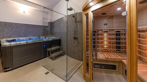 Een moderne spa met een glazen hottub, een aparte stoomruimte met houten banken en een betegelde douchehoek.