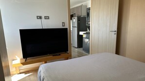 A bedroom with a bed, a TV on a wooden stand, and a kitchen in the background. - 4Grados Sur Guatemala City zona 4 Rooftop view (Ciudad de Guatemala)