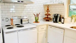 Et moderne køkken med hvide skabe, indbygget ovn, kaffemaskine og en dekorativ plante.