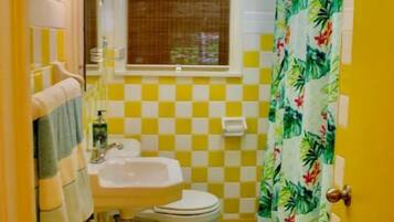 Un baño con pared a cuadros amarillo y blanco, un inodoro, un lavamanos y una cortina de ducha con motivos tropicales.