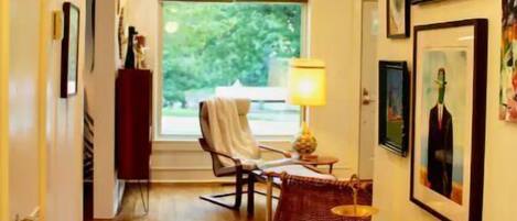 A hallway with wooden flooring, a dining area with a table and chairs, and a window with a view of greenery.