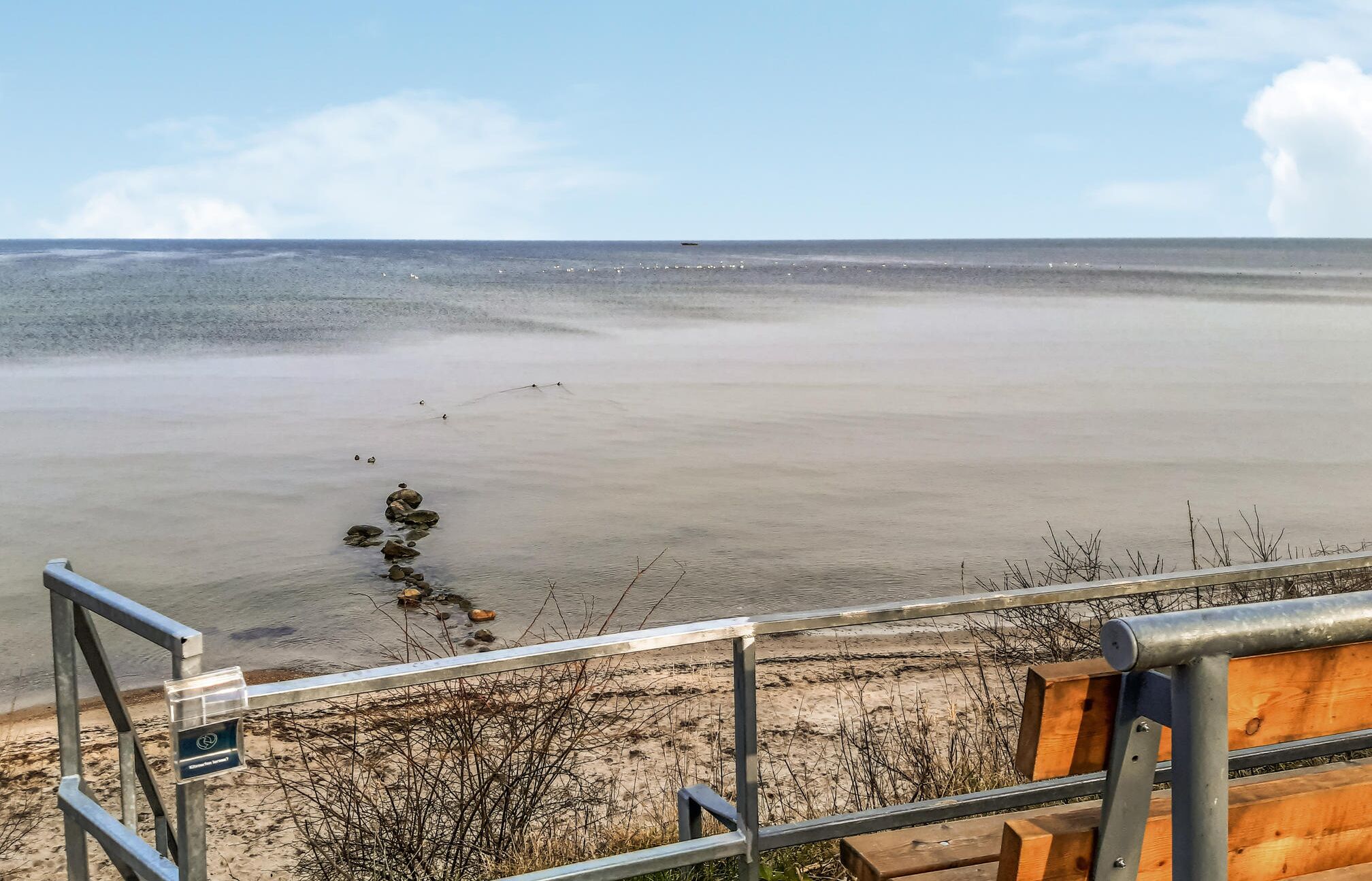 A beach with a metal railing and a wooden bench.