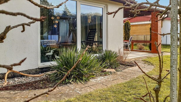 Ein Haus mit Terrasse, kleinem Garten und einer roten Backsteinmauer.