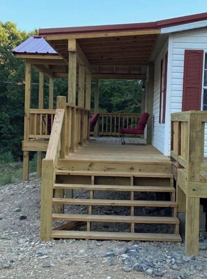 A wooden deck with a covered porch, a red chair, and a small table. - The Ranch House (Story)