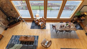 A spacious room with a large wooden table, a comfortable sofa, and a rocking chair. There is a telescope on a tripod in the corner, and a dining area with chairs. - Modern Chalet with Lake Views in Marina Area (Mossyrock)
