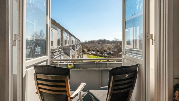 En balkong med två stolar och ett bord, med utsikt över ett bostadsområde med hus och en grön gräsmatta.