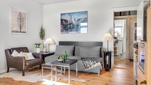 Ett modernt vardagsrum med en grå soffa, en fåtölj i läder, ett soffbord och en tavla som föreställer ett landskap.