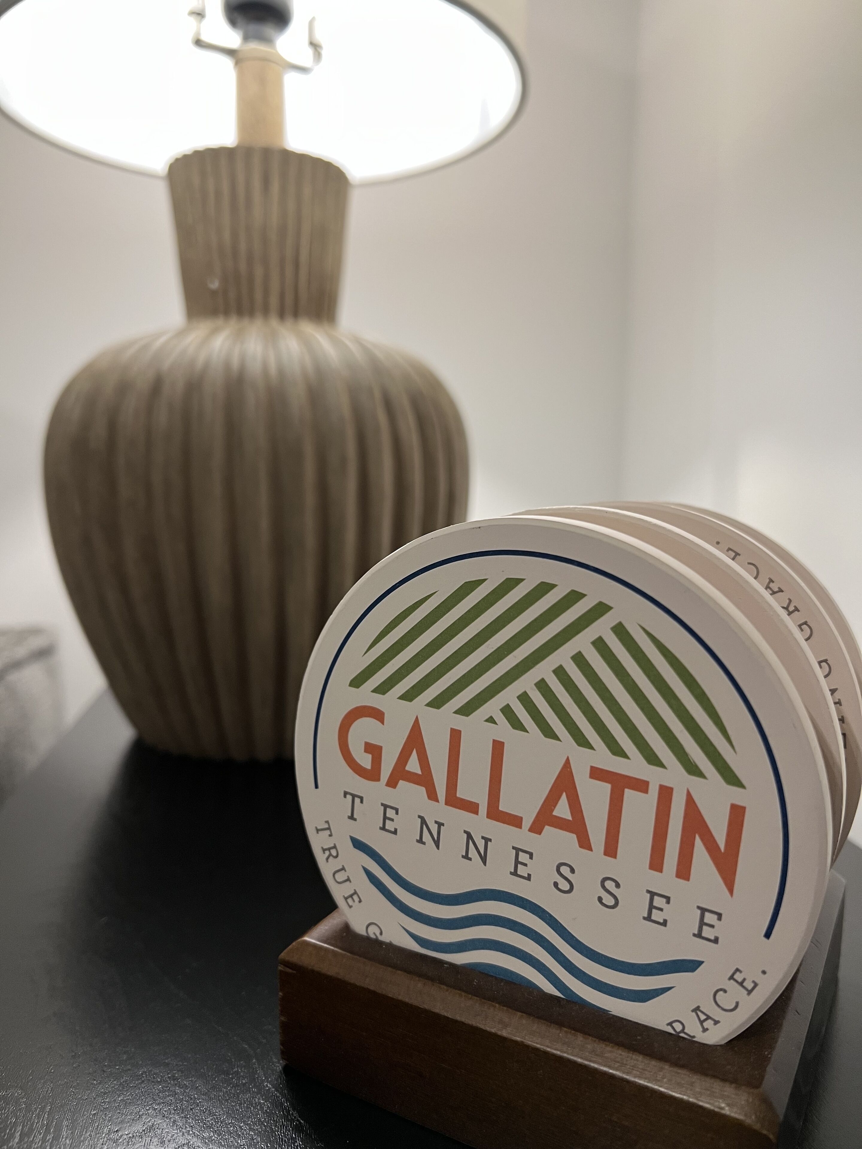 A coaster with "Gallatin Tennessee" text and a logo, placed on a wooden stand.