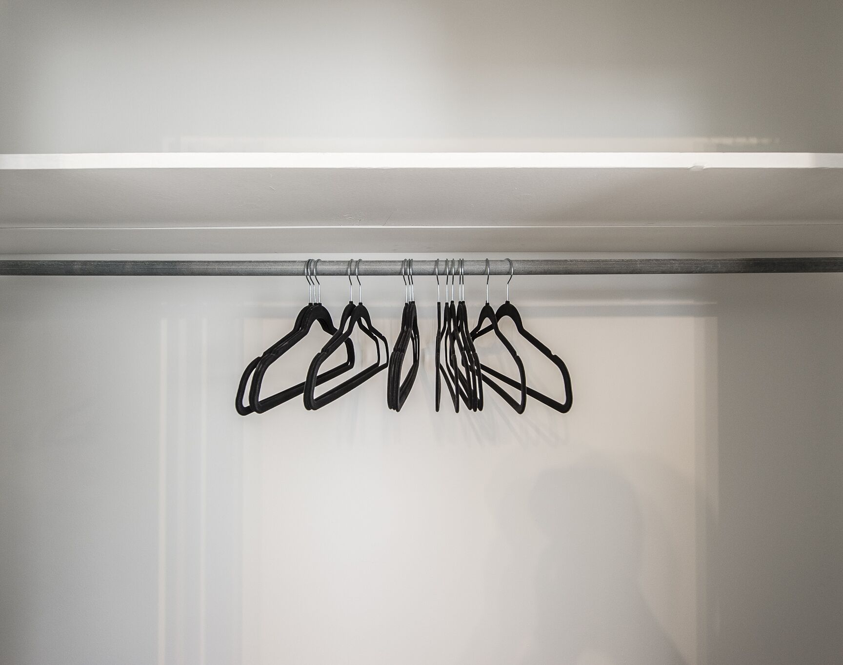 A closet with a rod holding multiple black hangers.