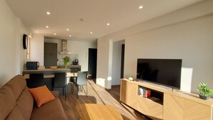 A modern living room with a sofa, a TV on a wooden stand, and a kitchen in the background. - Fréjus-Plage, Sea view, T2, 38m2, 4 people, refurbished, air conditioning, magnificent (Fréjus)