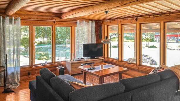 A cozy living room with a wooden ceiling, large windows, a flat-screen TV, a sofa, and a coffee table. - Amazing home in Arboga with sauna (Arboga)