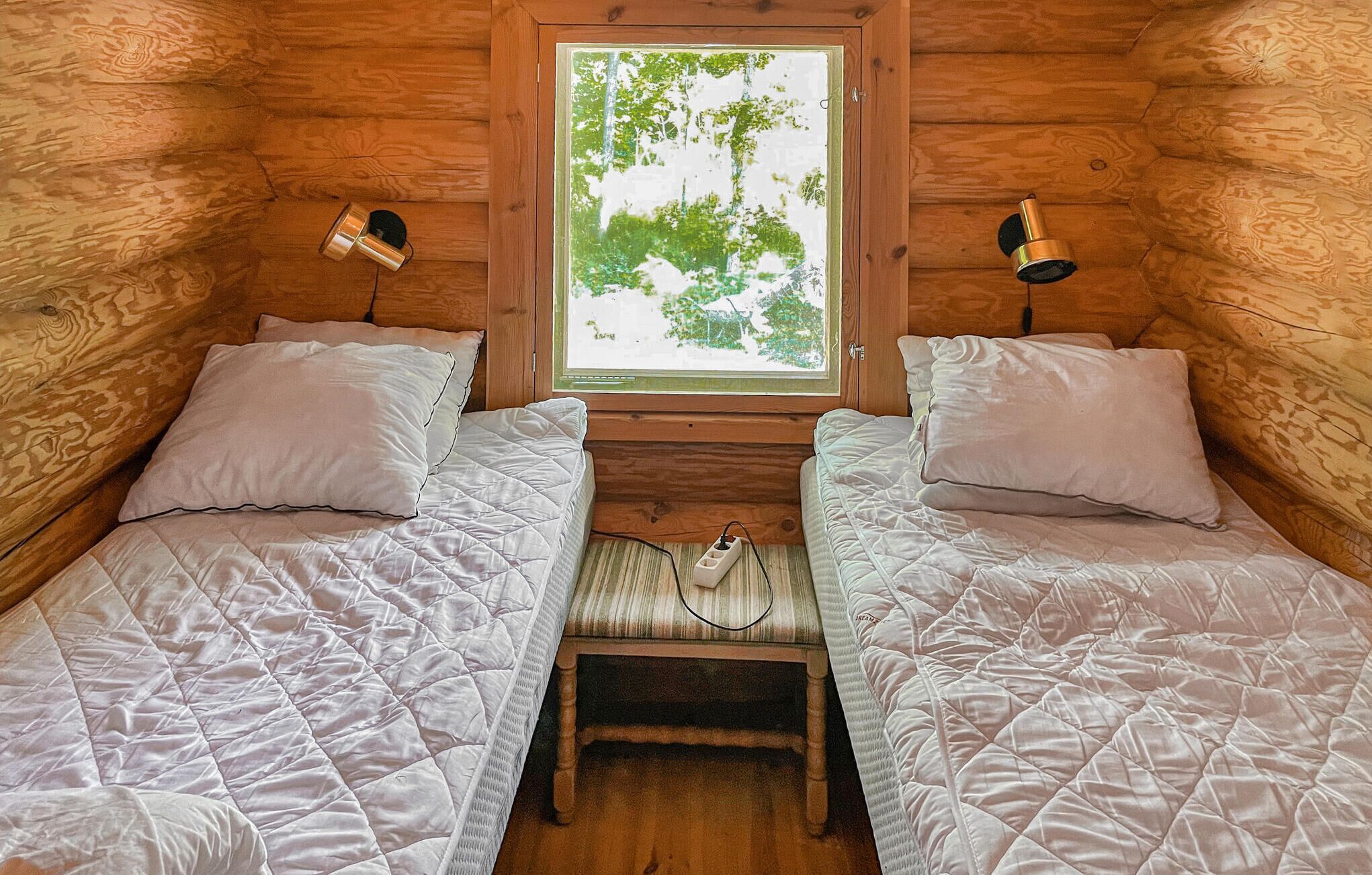 A cabin with two beds, a window with a view of trees, and two wall-mounted lamps.