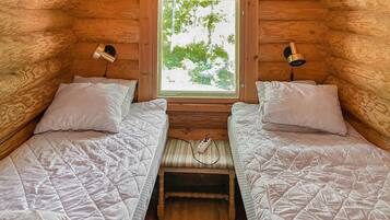 A cabin with two beds, a window with a view of trees, and two wall-mounted lamps.