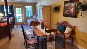 Un comedor con una mesa de madera, sillas y un banco. Hay una puerta que da a otra habitación y una ventana con cortinas.
