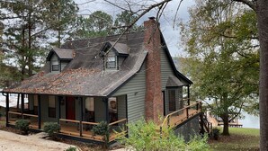 Una casa de dos pisos con un porche cubierto, una chimenea de ladrillo y vista a un lago.