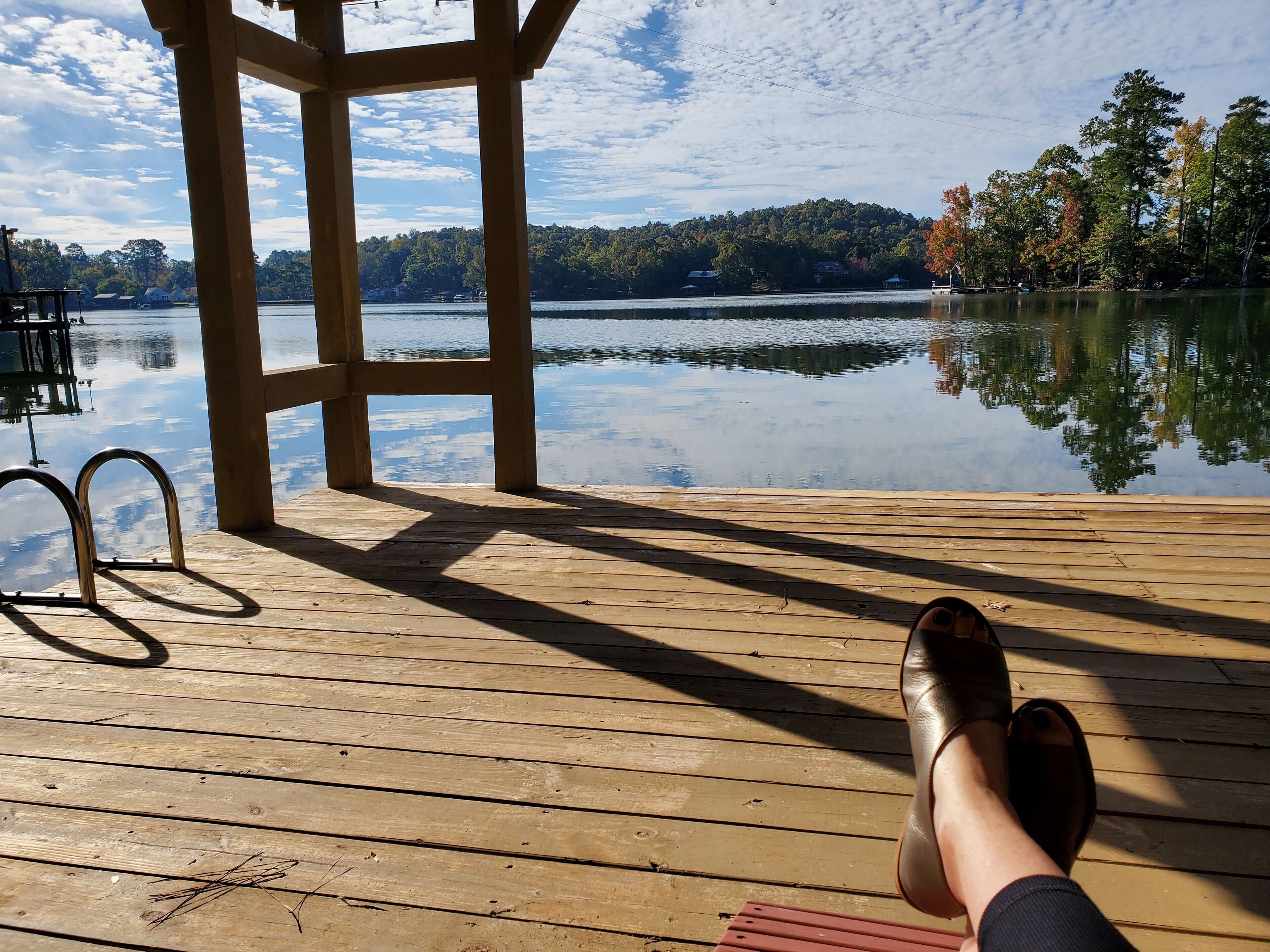 Una terraza de madera con vistas despejadas a un lago tranquilo y colinas boscosas al fondo.