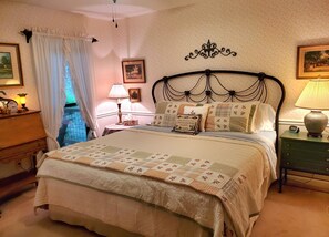 A bedroom with a large bed, a nightstand with a lamp, a dresser, and a window with curtains.