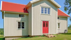 Una casa de madera de dos pisos con techo y puerta principal de color rojo.